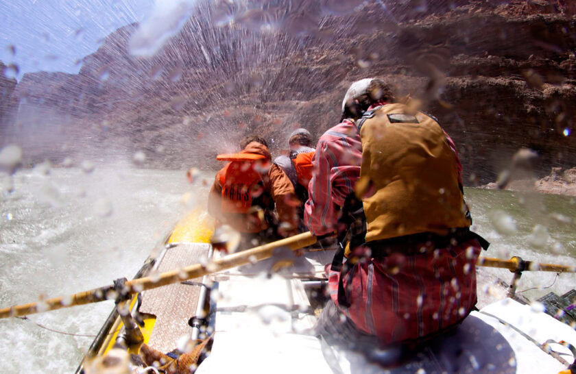 Guide and guests put heads down as they splash through wave on OARS river trip in Grand Canyon