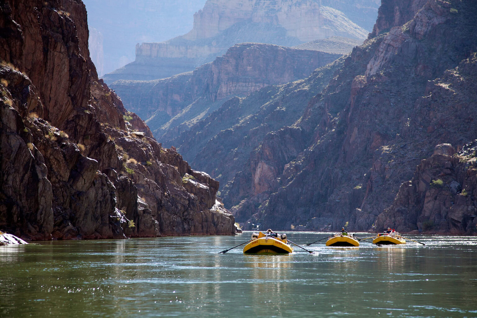 Three OARS yellow rafts row towards camera in calm water in Grand Canyon