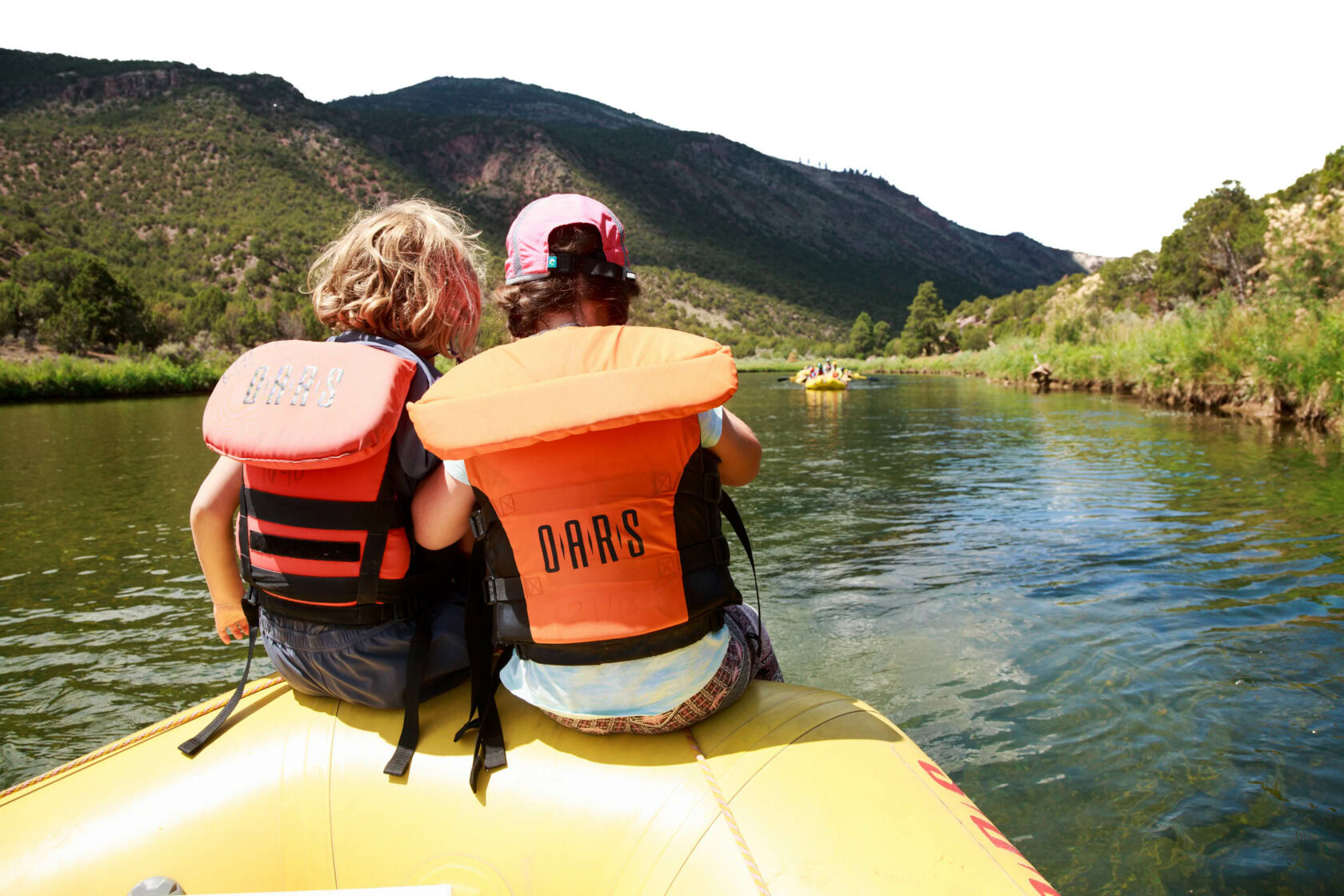 Two kid sitting side by side on a raft on the river.