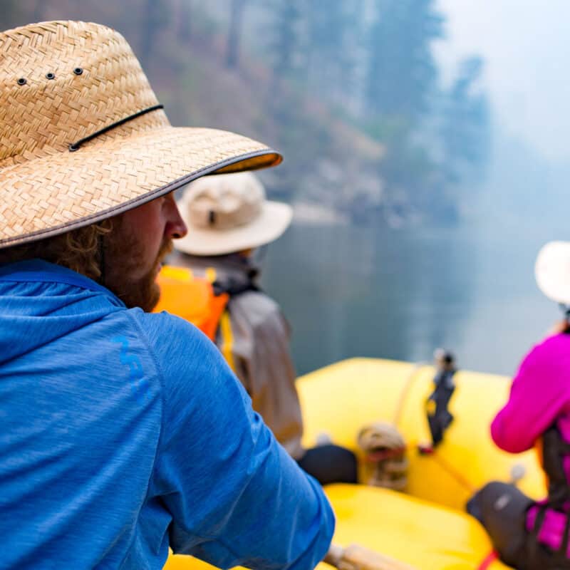 3 people in a raft rowing down a river.