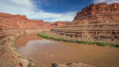 Aerial view of the Colorado River with several tiny, bright yellow rafts floating downstream