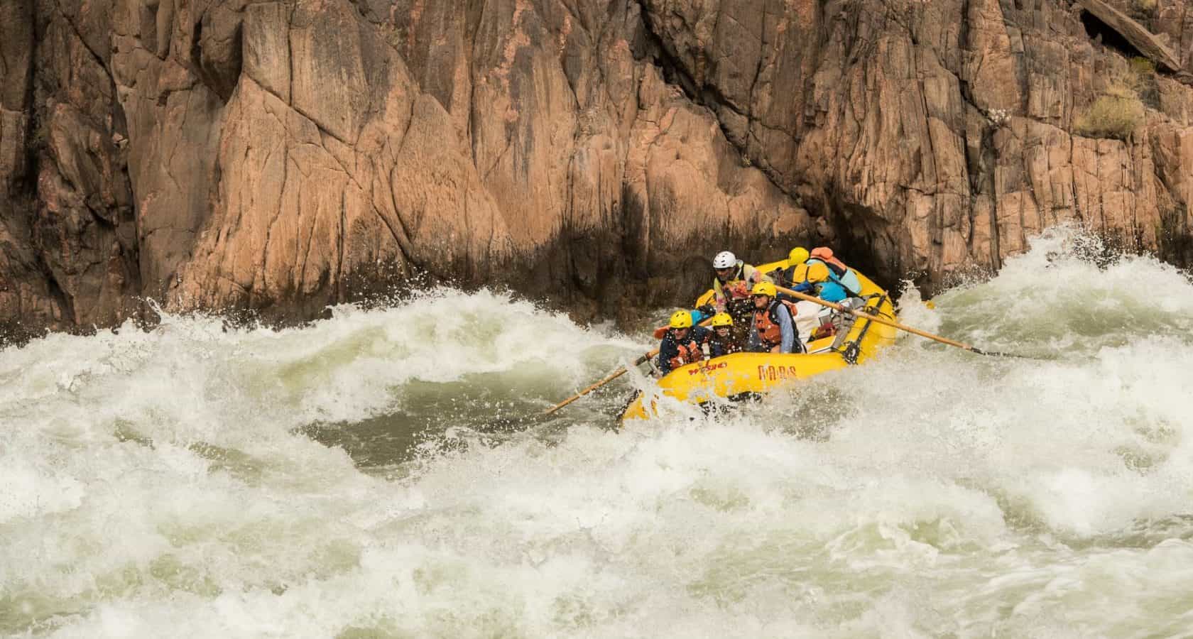 Guests on a Grand Canyon rafting trip ride a raft through a huge wave