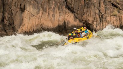 Guests on a Grand Canyon rafting trip ride a raft through a huge wave